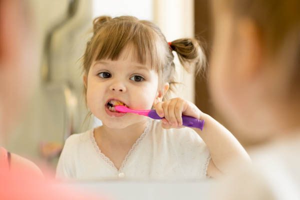 Cute child girl looking at mirror using toothbrush cleaning teeth in bathroom every morning and night.